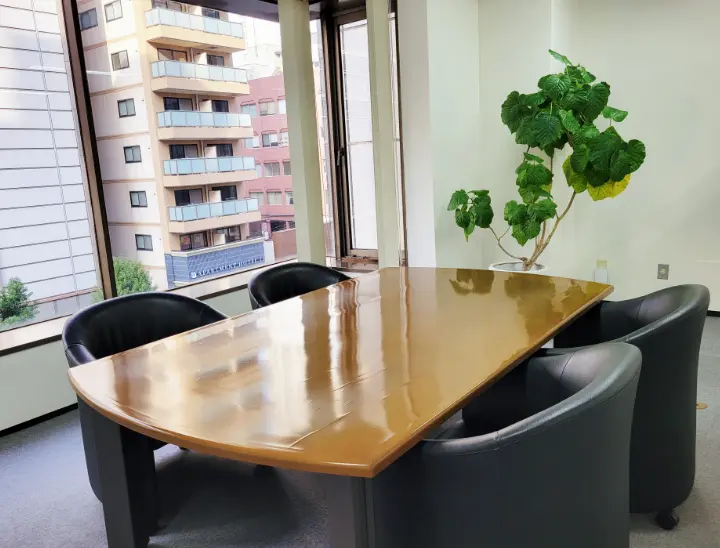 明るい窓際にある木目調のテーブルが置かれた応接室・面談スペース